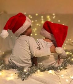 two babies wearing santa hats on top of a white sheet covered in tinsel lights