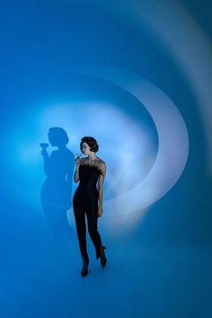 a woman standing in front of a blue wall with a shadow on it's face