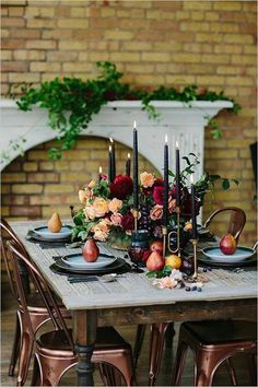 the table is set with candles, fruit and flowers in front of a brick wall