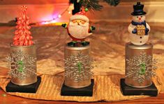 three tin cans with santa claus and snowmen on them sitting next to a christmas tree