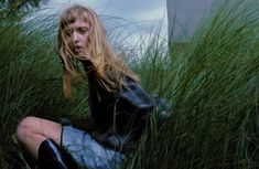 a woman sitting in tall grass with her hair blowing in the wind and looking at the camera