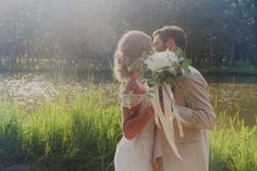 a bride and groom standing next to each other in front of a lake with flowers