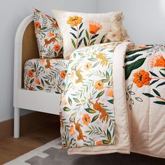 a white bed with orange flowers and green leaves on the comforter next to it