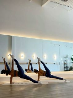 three women doing yoga poses on their stomachs in an empty room with mirrors behind them