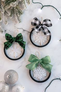 three ornaments with bows and snowflakes are on a marble surface next to christmas decorations