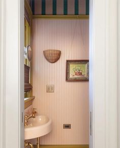 an open door leading to a bathroom with a pedestal sink and striped wallpaper on the walls