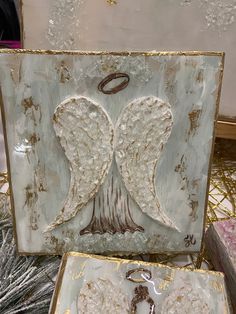 two white angel wings are on display in front of a gold and silver box with a keychain hanging from it