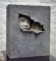 a sculpture with two faces in the middle of it's face, and another piece of concrete behind it