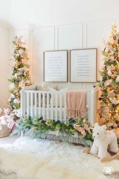 a white crib in front of christmas trees with two framed pictures on the wall