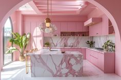 a kitchen with pink walls and marble counter tops, along with an archway leading to the dining room