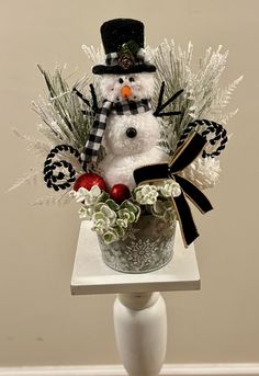 a snowman is sitting on top of a vase filled with flowers and greenery