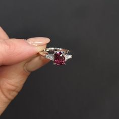 a person holding a ring with a pink stone in it