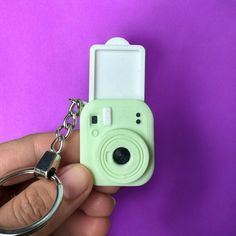 a person holding a camera keychain in their left hand with a purple background