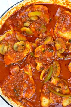 a pan filled with meat and vegetables covered in sauce on top of a white table