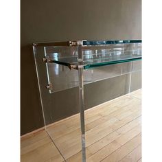 a clear glass table with metal legs on wooden floor in front of a gray wall