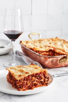 a slice of lasagna on a plate next to a glass of red wine