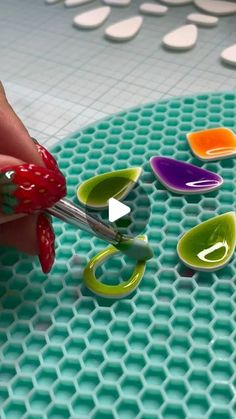 someone using scissors to cut glass circles on a surface with holes in the middle that are colored green, red, orange and purple