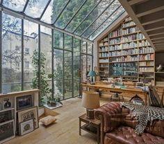 a living room filled with lots of books and furniture next to a large glass window