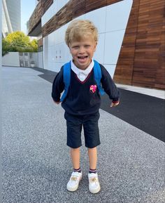 a little boy that is standing in the street with his hands in his pockets and smiling