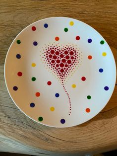 a white plate with multicolored dots and a red heart on the center is sitting on a wooden table