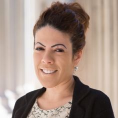 a woman smiling and wearing a black cardigan over a floral top with her hair in a bun