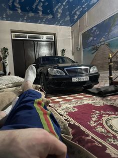 a person's feet resting on a rug in front of a black mercedes car