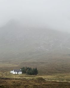 a white house in the middle of a field with mountains in the background on a foggy day