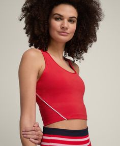 a woman with curly hair wearing a red top and striped skirt