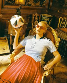 a woman sitting in a chair with a soccer ball on her hand and wearing sunglasses