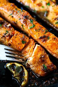 grilled salmon on a black plate with a fork and lemon wedges next to it