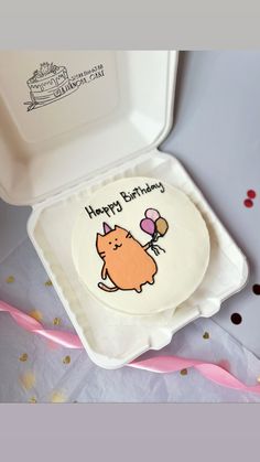 a birthday cake in a white box with a cartoon cat on the front and balloon attached to it