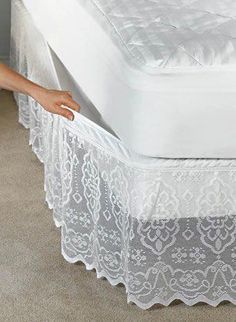 a bed with white lace on it and a person holding the edge of it in their hand