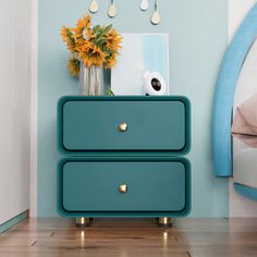 a blue dresser with two drawers in a bedroom next to a bed and flowers on the nightstand