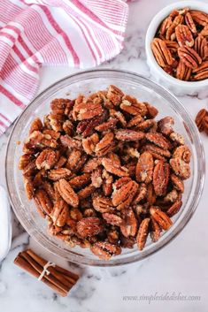 a bowl filled with nuts next to cinnamon sticks and an orange striped dish towel on top of a marble counter