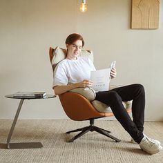 a woman sitting in a chair holding a piece of paper and looking at her phone