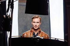 a man standing in front of a camera with his head turned to the side and wearing a leather jacket