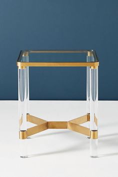 a glass and gold end table on a white surface with a blue wall in the background