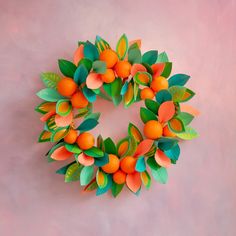 an origami wreath with oranges and leaves hanging on a pink wall in the shape of a circle