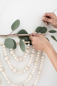 two hands are working on a string of wood beads and greenery that is attached to the wall