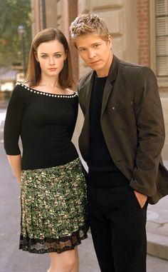 two people standing next to each other in front of a building and looking at the camera