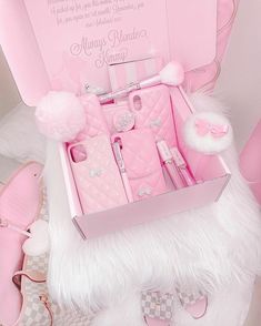 a pink box filled with lots of items on top of a white bed covered in fur