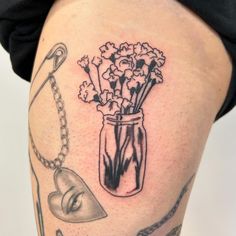 a woman's thigh with tattoos and flowers in a jar