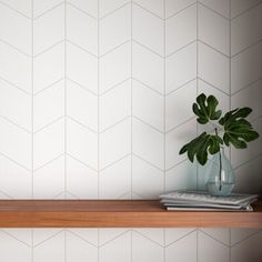 a wooden shelf with a plant on top of it next to a white tiled wall