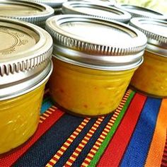 several jars filled with yellow liquid sitting on top of a colorful table cloth next to each other