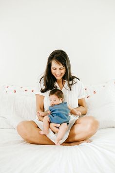 a woman sitting on top of a bed holding a baby