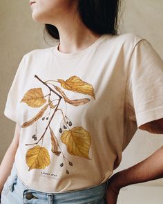 T-shirt featuring a botanical illustration of fall Linden tree (Tilia cordata). Fall in love with our autumn leaves shirt that you won't find anywhere else. Printed on a cream t-shirt, made from durable lightweight cotton. Unisex fit - boxy and long. How it's made: * All prints are original watercolor designs hand-painted by a botanical artist. * Ethically made 100% cotton t-shirts that are made to last. * T-shirts are printed and shipped by my printing partner in the US, Canada, or Europe. * By buying from this shop you are directly supporting a woman-owned small business, created out of love for plants to educate, inspire and keep us connected to the natural world. About the artist: This Shop is an extension of my botanical illustration studio, where I create hand-painted watercolor art Fall Crew Neck T-shirt With Plants Print, Crew Neck Cotton T-shirt With Watercolor Print, Botanical Relaxed Fit Tops For Fall, Graphic Tee With Watercolor Print In Cotton, Relaxed Fit Graphic Tee With Watercolor Print, Relaxed Fit Watercolor Print Graphic Tee, Fall Cotton T-shirt With Plants Print, Fall Plants Print Cotton T-shirt, White T-shirt With Fall Themed Plant Print