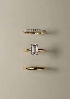 three gold rings with an emerald cut diamond in the middle and side stones on each band