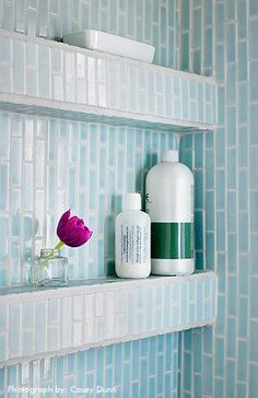 two white shelves with bottles and vases on them in a blue tiled bathroom area