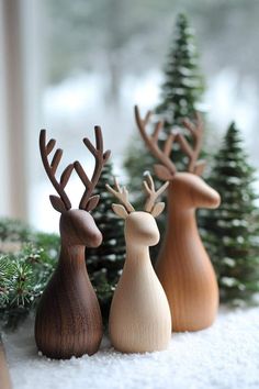 three wooden reindeer figurines sitting next to each other in front of pine trees