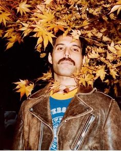 a man with a moustache standing in front of a tree filled with leaves